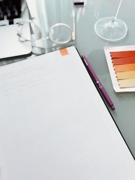A minimalist office desk setup featuring a notebook, colored swatches, and a purple pen.