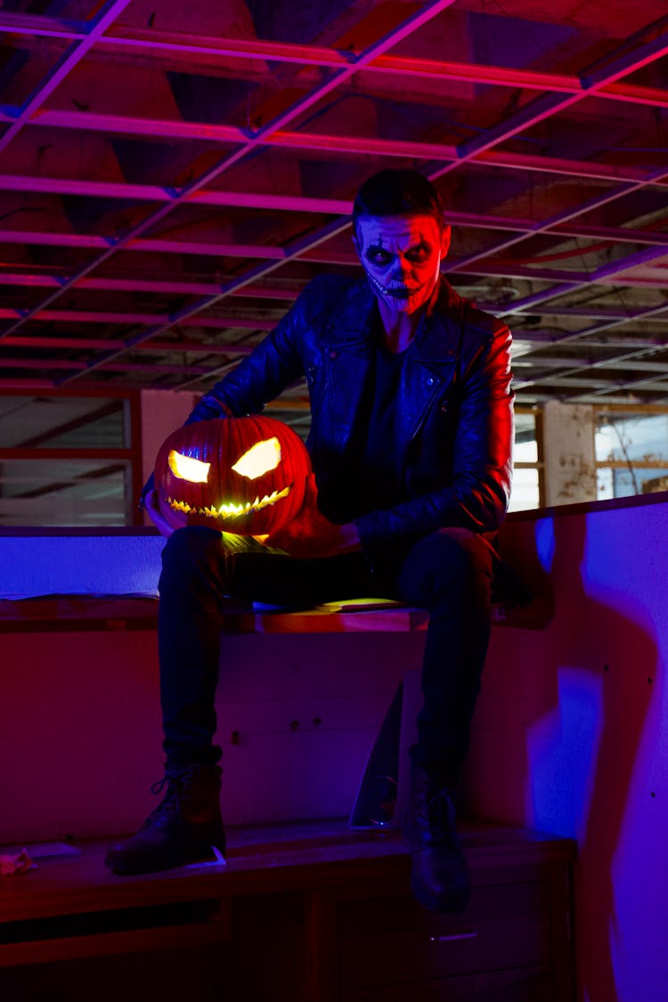 A Man In A Creepy Face Paint Holding A Jack O Lantern