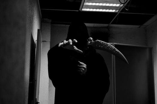 A shadowy figure in a hooded cloak reaches out, holding a scythe in a dimly lit room.