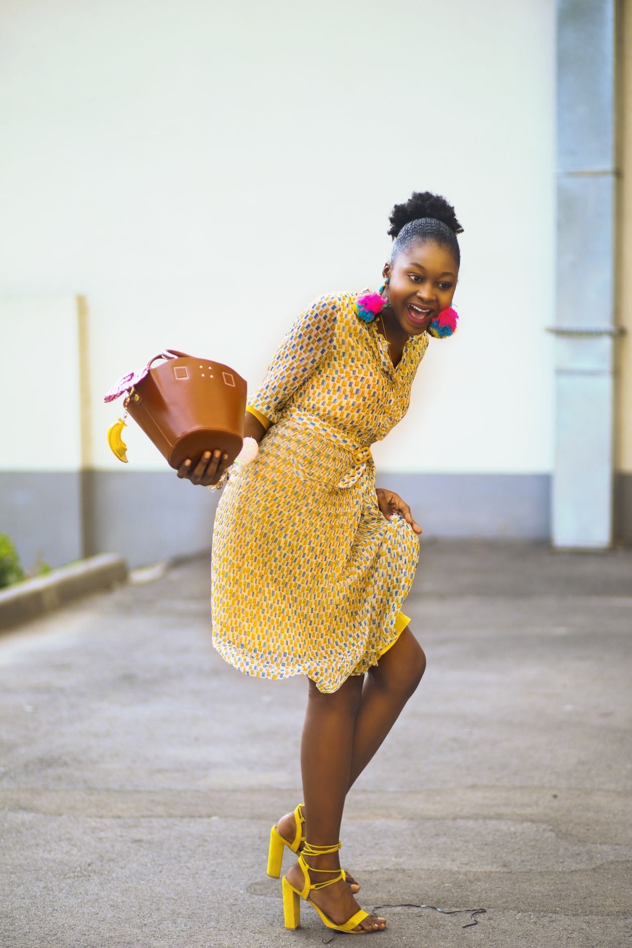 Smiling woman in a yellow patterned midi dress with yellow block heels and a brown handbag