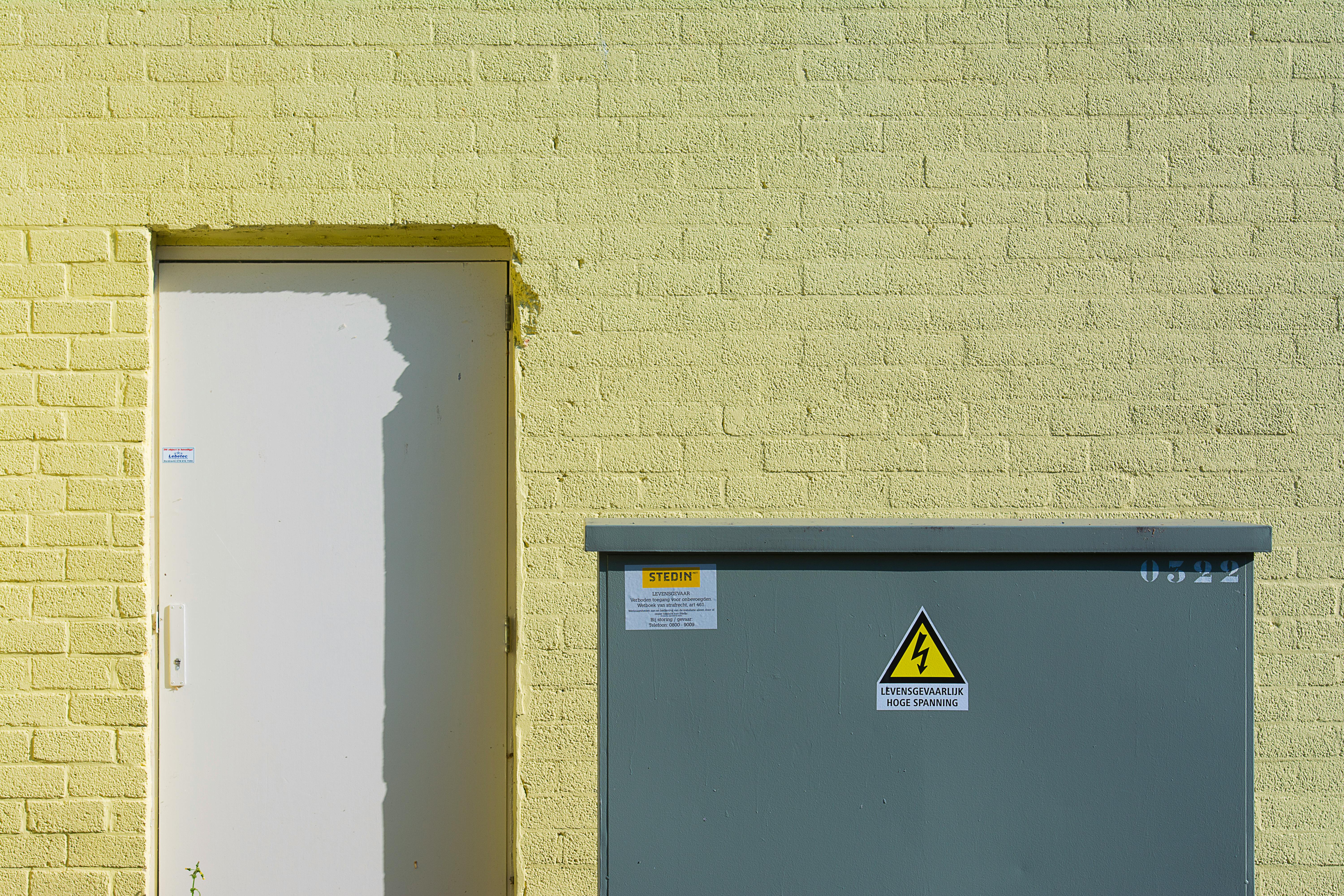 A sunlit yellow brick wall with a white door and an electrical box, creating a modern industrial look.