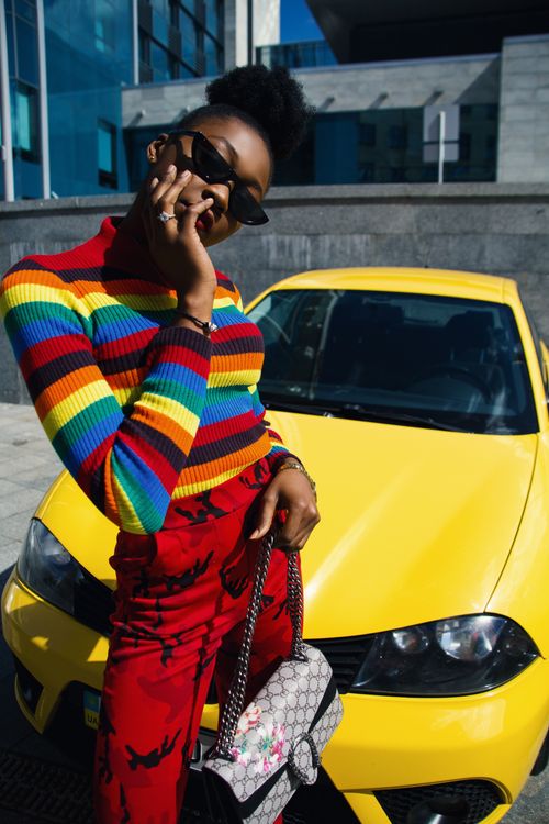 Free Stylish woman posing in vibrant outfit with a yellow car on a sunny day. Stock Photo