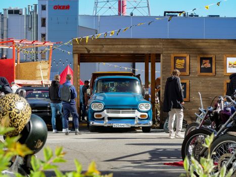 A vibrant outdoor festival showcasing vintage cars and motorcycles with people enjoying the sunny day.