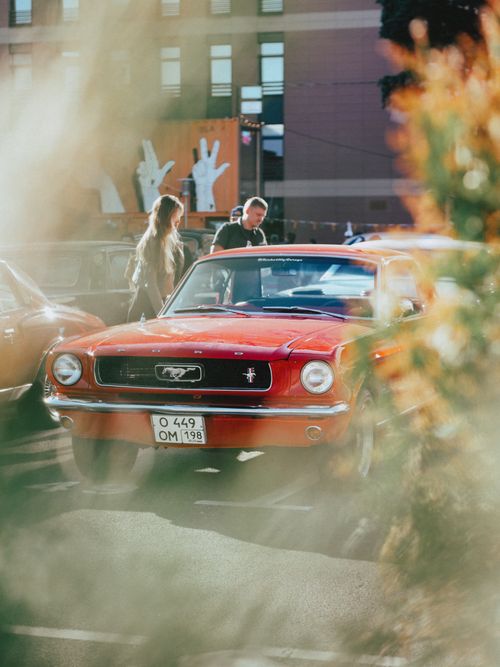 Free A classic red Ford Mustang parked outdoors with people nearby in a city setting. Stock Photo