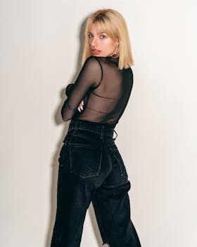 Stylish young woman in a sheer black blouse posing confidently in a studio setting.