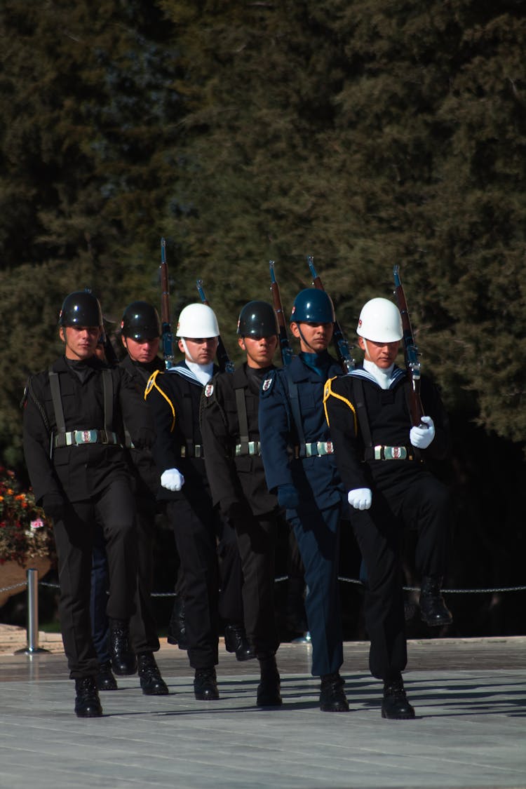 A Group Of Men In Black Uniforms Marching With Riffles