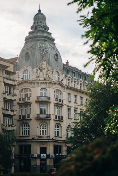Free A beautifully ornate historic building framed by lush greenery and a cloudy sky. Stock Photo