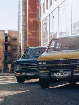 Two classic vans with Russian plates parked in a sunlit urban area.