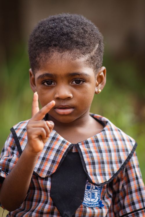 Free Cute young child in a plaid school uniform showing a V sign gesture outdoors. Stock Photo