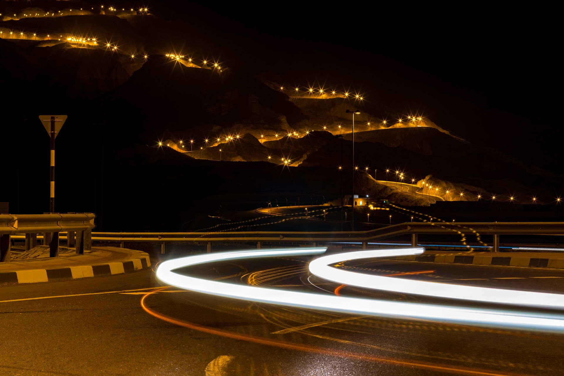 Long exposure of a winding road and hillside highlighted by streetlights at night.