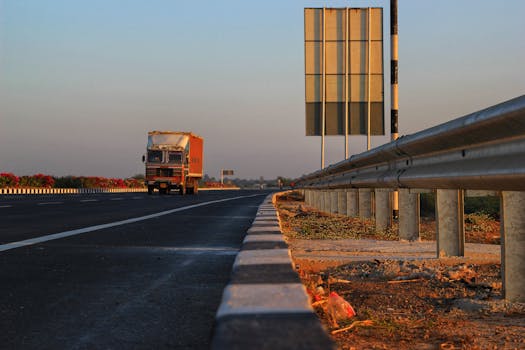 A solitary truck travels down a deserted highway at sunset, with clear blue skies overhead.