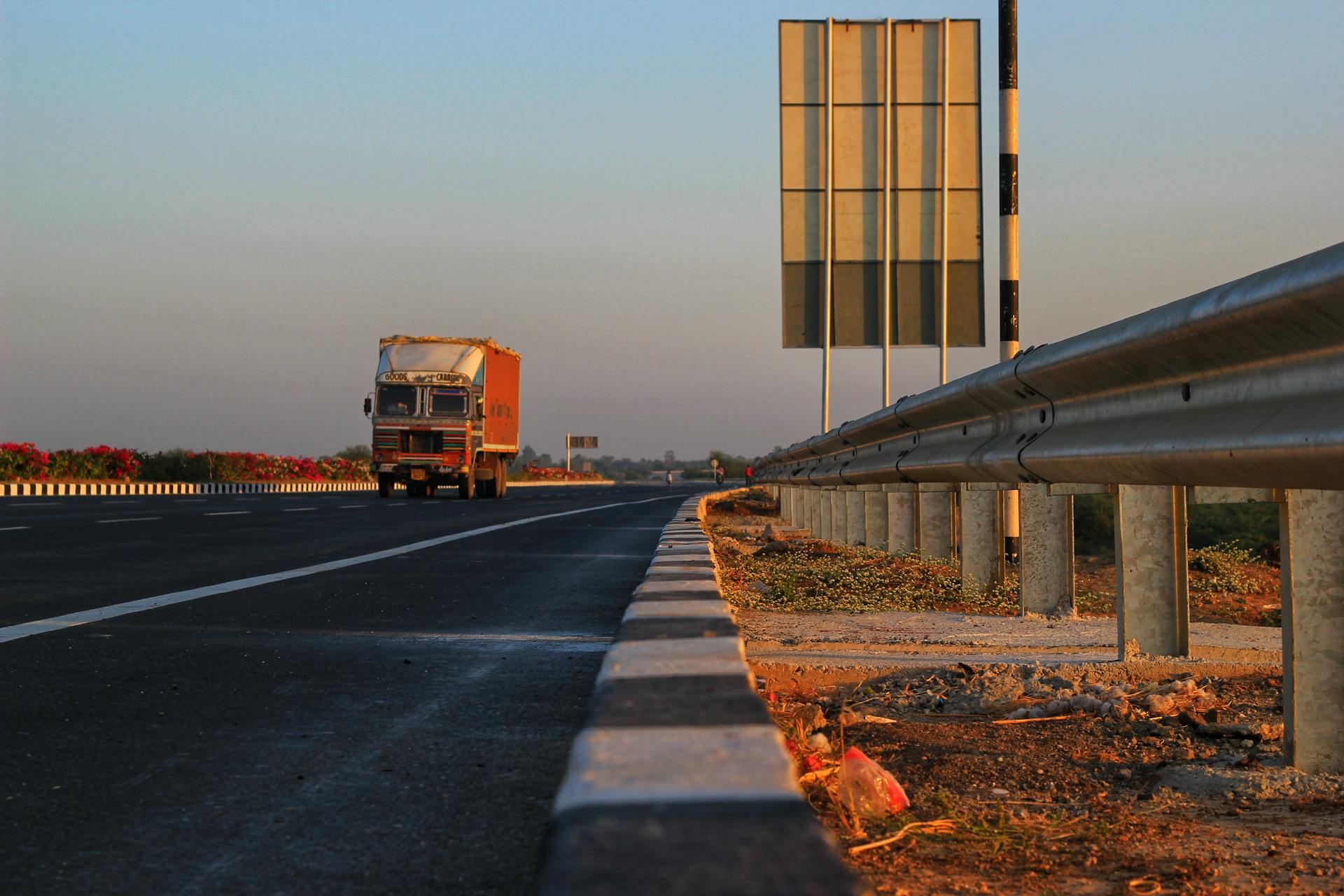 A solitary truck travels down a deserted highway at sunset, with clear blue skies overhead.