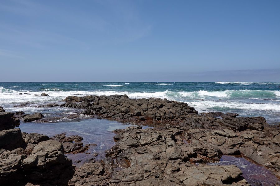 Stunning view of rocky shoreline with crashing waves under a clear blue sky.