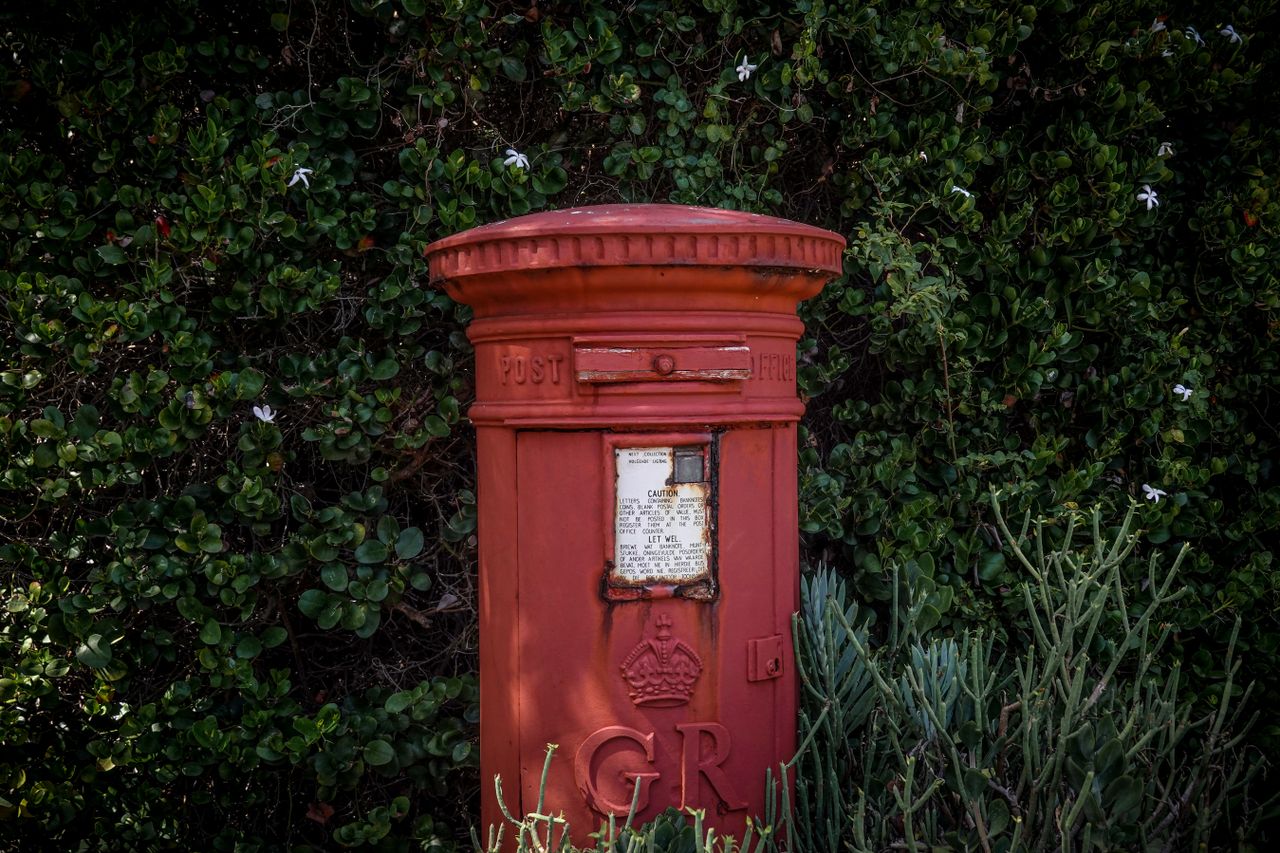a classic red postbox surrounded by lush green bushes capturing vintag
