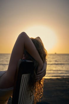 A woman sitting on a beach chair, enjoying a serene sunset by the sea.