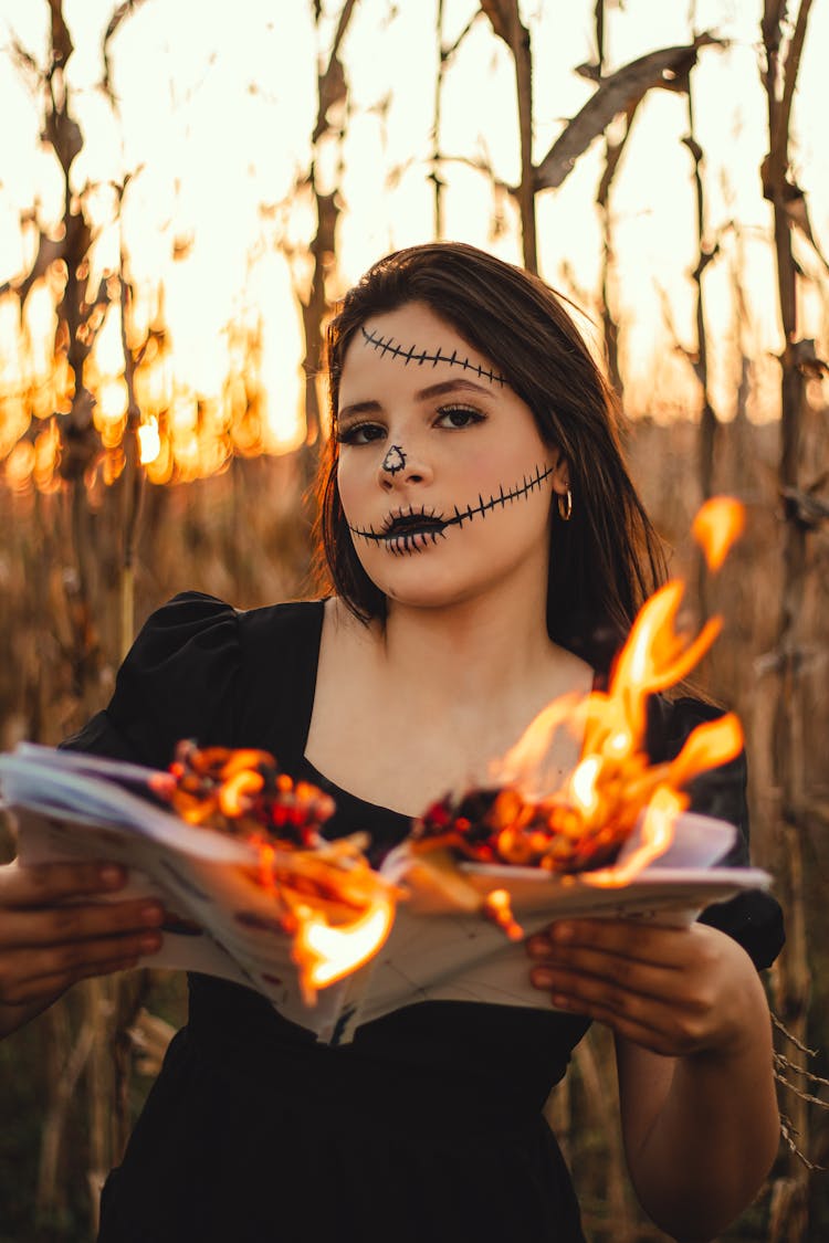 Girl With Halloween Makeup With Burning Paper In Hands