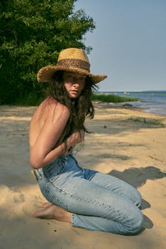 Woman in denim jeans and straw hat posing on a sunny beach day.