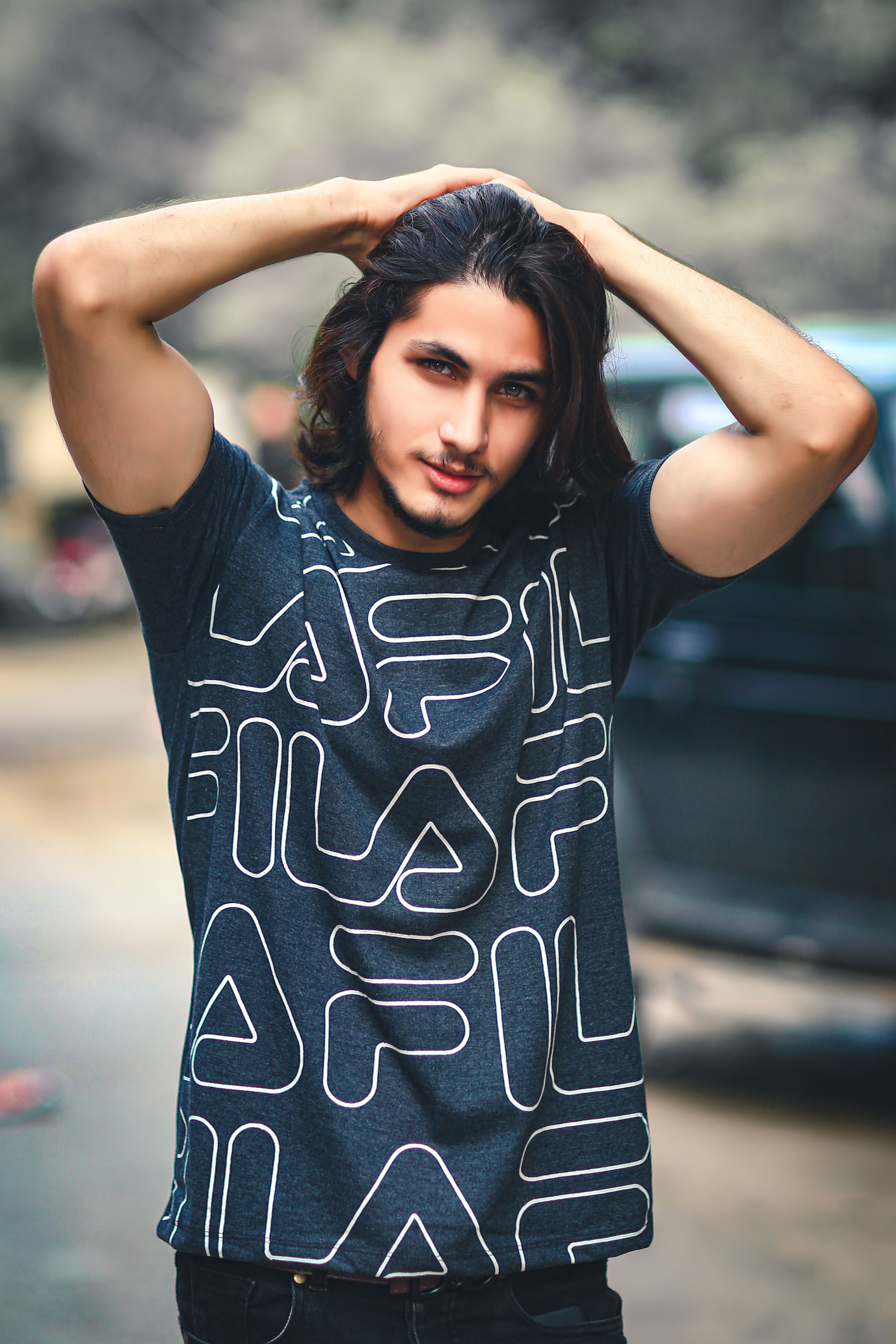 Portrait of a bearded young man in a printed shirt posing outdoors with hands in hair.