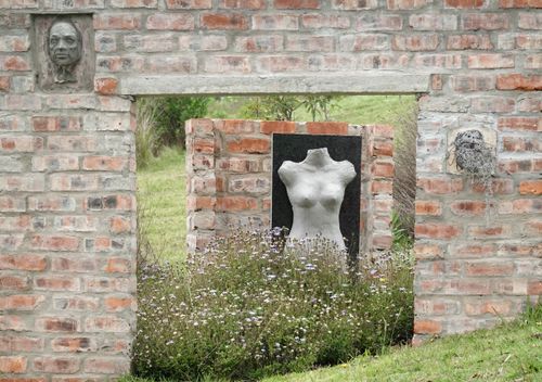 Free Brick wall with sculptures in an outdoor garden setting, surrounded by flowers. Stock Photo