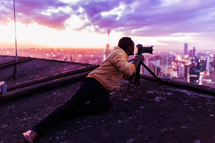 Photographer on a Rooftop Taking Photo of a Cityscape at Dusk 