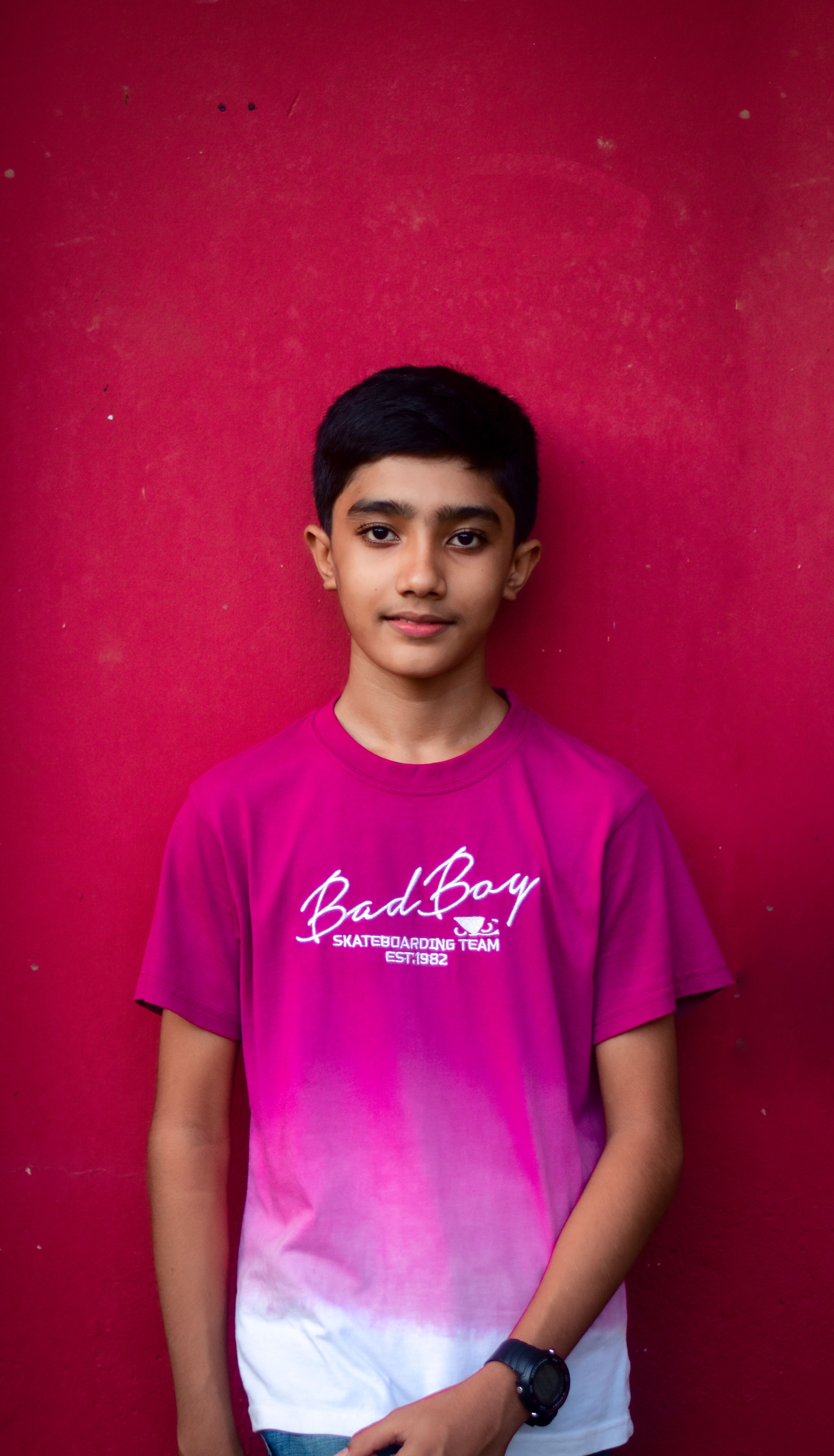 Portrait of a trendy teenage boy in a gradient t-shirt standing against a vibrant red wall.