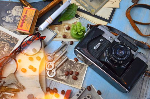 Retro flatlay with vintage camera, old photos, eyeglasses, and keys on a table.