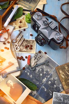 一台老式相机平放着，周围散落着旧黑白照片、钥匙和咖啡豆