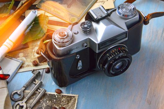 A classic film camera surrounded by nostalgic elements like keys, photos, and roasted coffee beans on a wooden table.