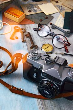 A vintage camera surrounded by glasses, keys, and old papers on a wooden table.