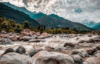 山间河流风景优美，流经岩石，背景是郁郁葱葱的树木和云层