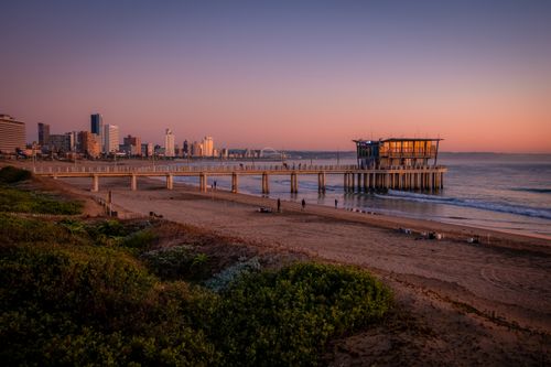 Free Captivating sunrise view of a beach and pier against a city skyline. Stock Photo