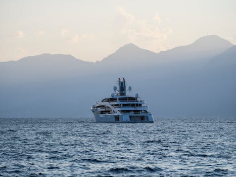 Elegant yacht sailing on calm sea waters against a tranquil mountain backdrop, showcasing luxury travel.