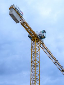 Yellow tower crane with metal structure against a cloudy blue sky.