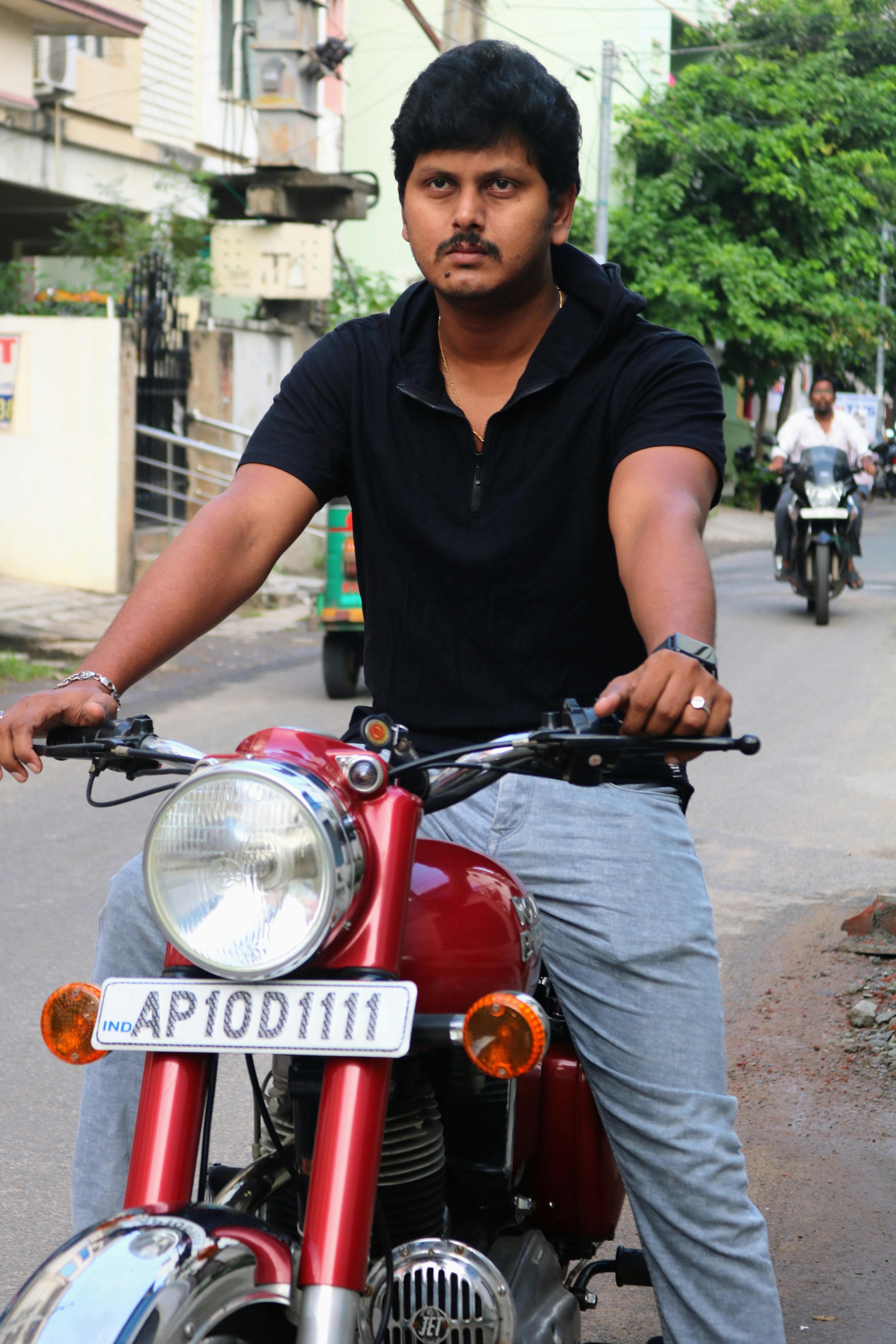 Man in black shirt riding a red motorcycle on a city street during the day.