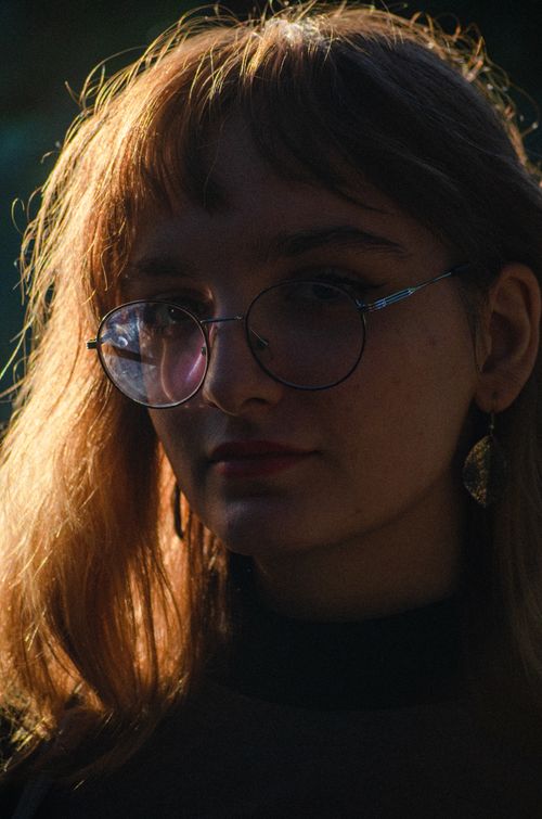 Free A portrait of a young woman wearing glasses, captured in dramatic lighting and deep shadows. Stock Photo