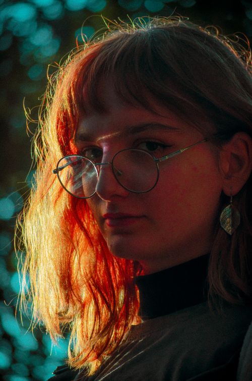 Free Close-up of a young woman wearing eyeglasses, captured in soft lighting with vivid colors, creating a moody atmosphere. Stock Photo