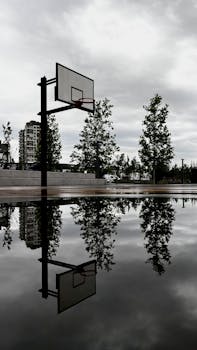 A serene view of a basketball court reflected in rainwater, captured on a cloudy day in Istanbul.