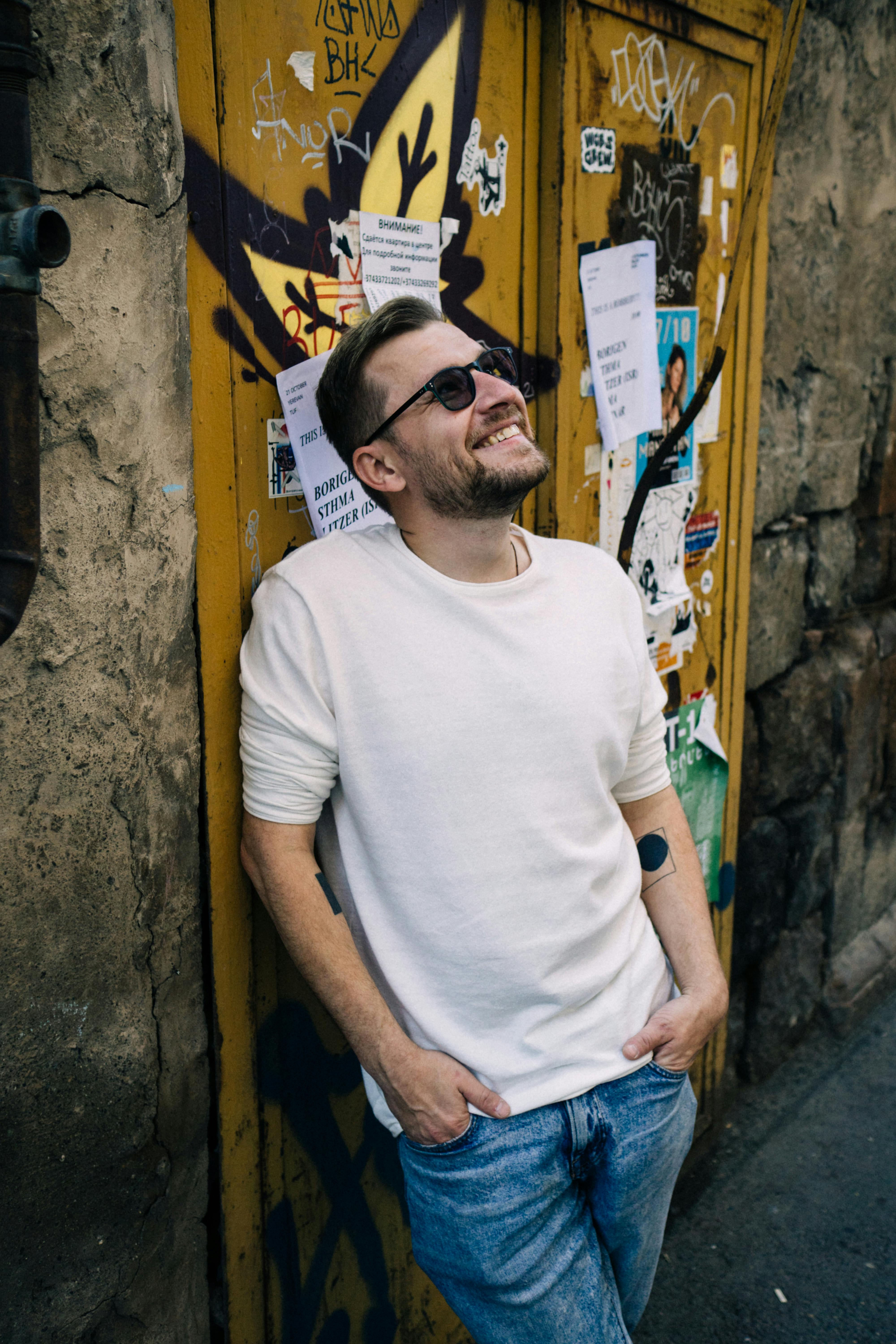 Portrait of a stylish man smiling against a graffiti-covered wall, embodying urban fashion and cool confidence.