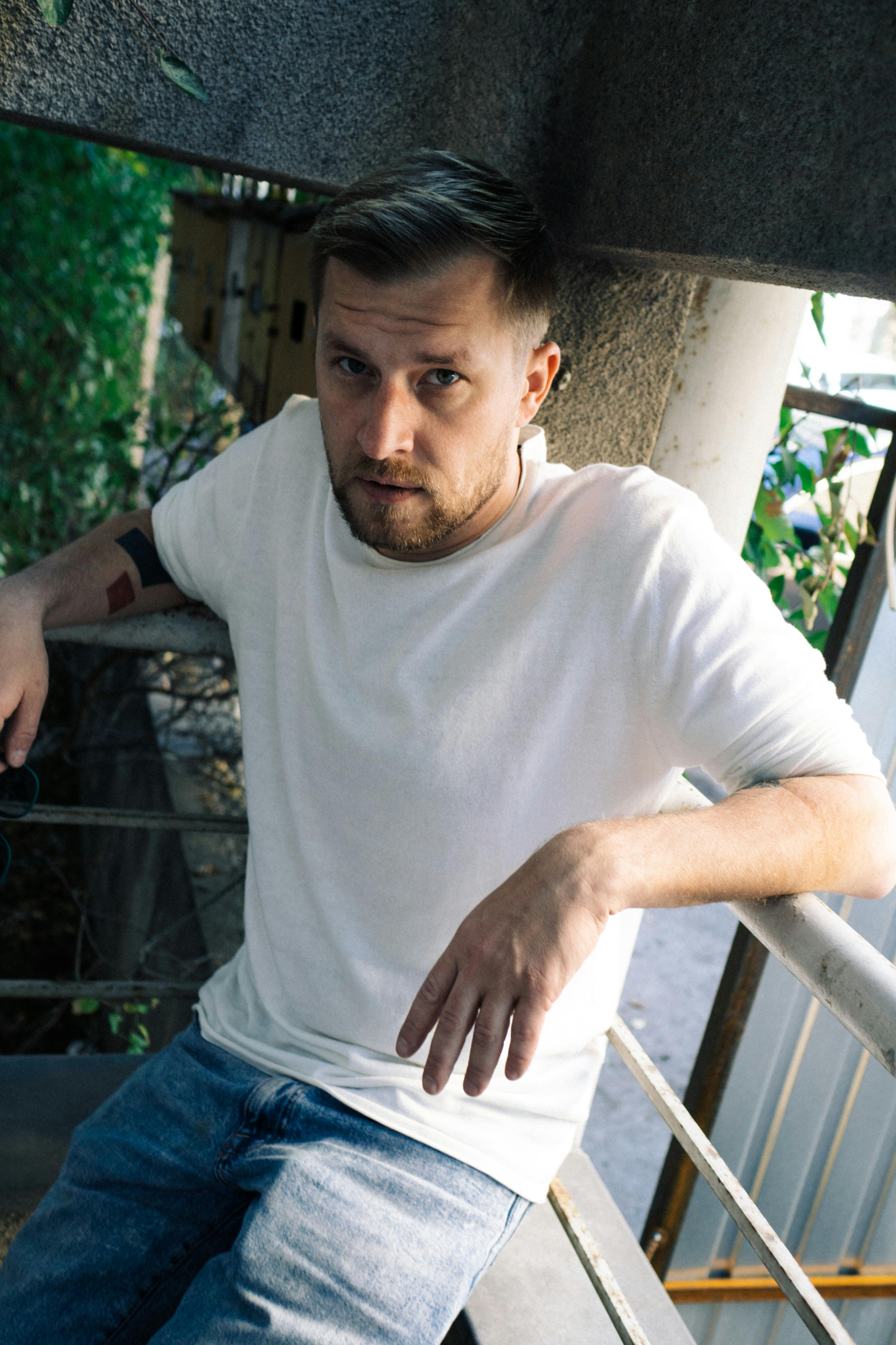 A bearded man poses casually on an urban balcony, conveying a relaxed outdoor vibe.