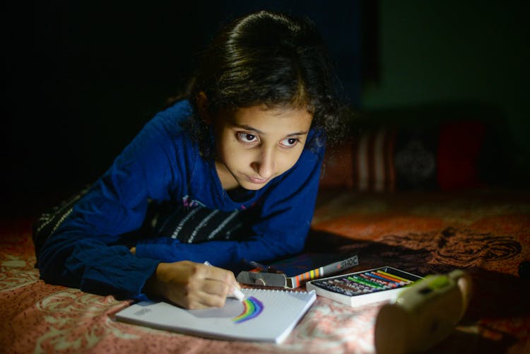 A Girl Drawing Rainbow On A Notebook