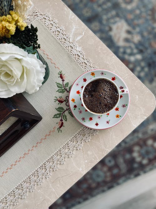 A Cup of Hot Chocolate Drink on the Edge of the Table Near White Flower