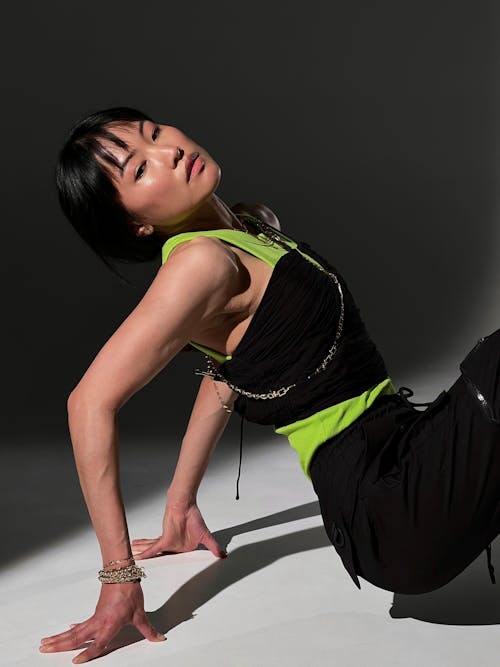 A Woman in Black Outfit Sitting on the Floor while Posing at the Camera