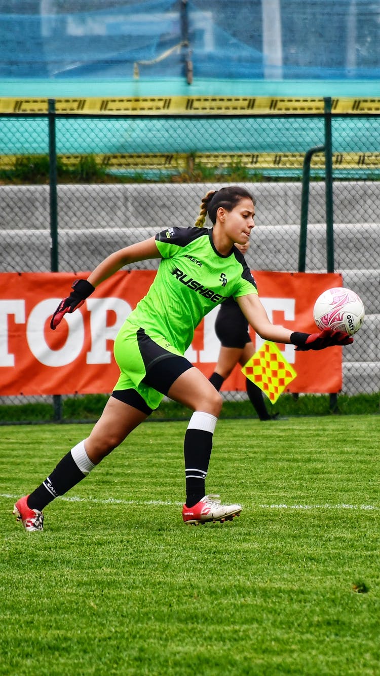 A Young Woman Holding Soccer Ball On Green Field