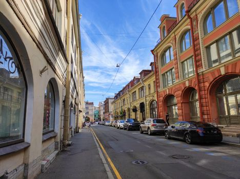 A vibrant city street showcasing historic architecture and parked cars under a bright blue sky.