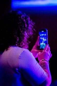 A person taking a photo in a vibrant blue and purple light setting.