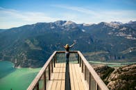 女人站在观景台上，张开双臂，俯瞰着令人惊叹的山脉和郁郁葱葱的景色