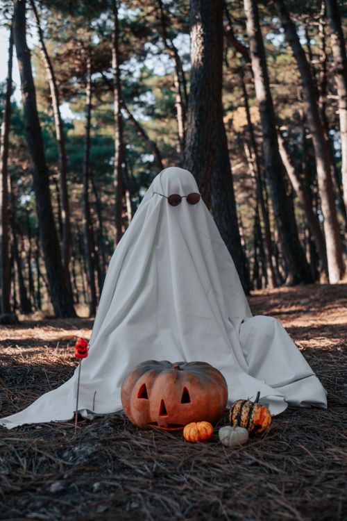 Free Eerie ghost costume with pumpkins in a dimly lit forest, perfect for Halloween theme. Stock Photo