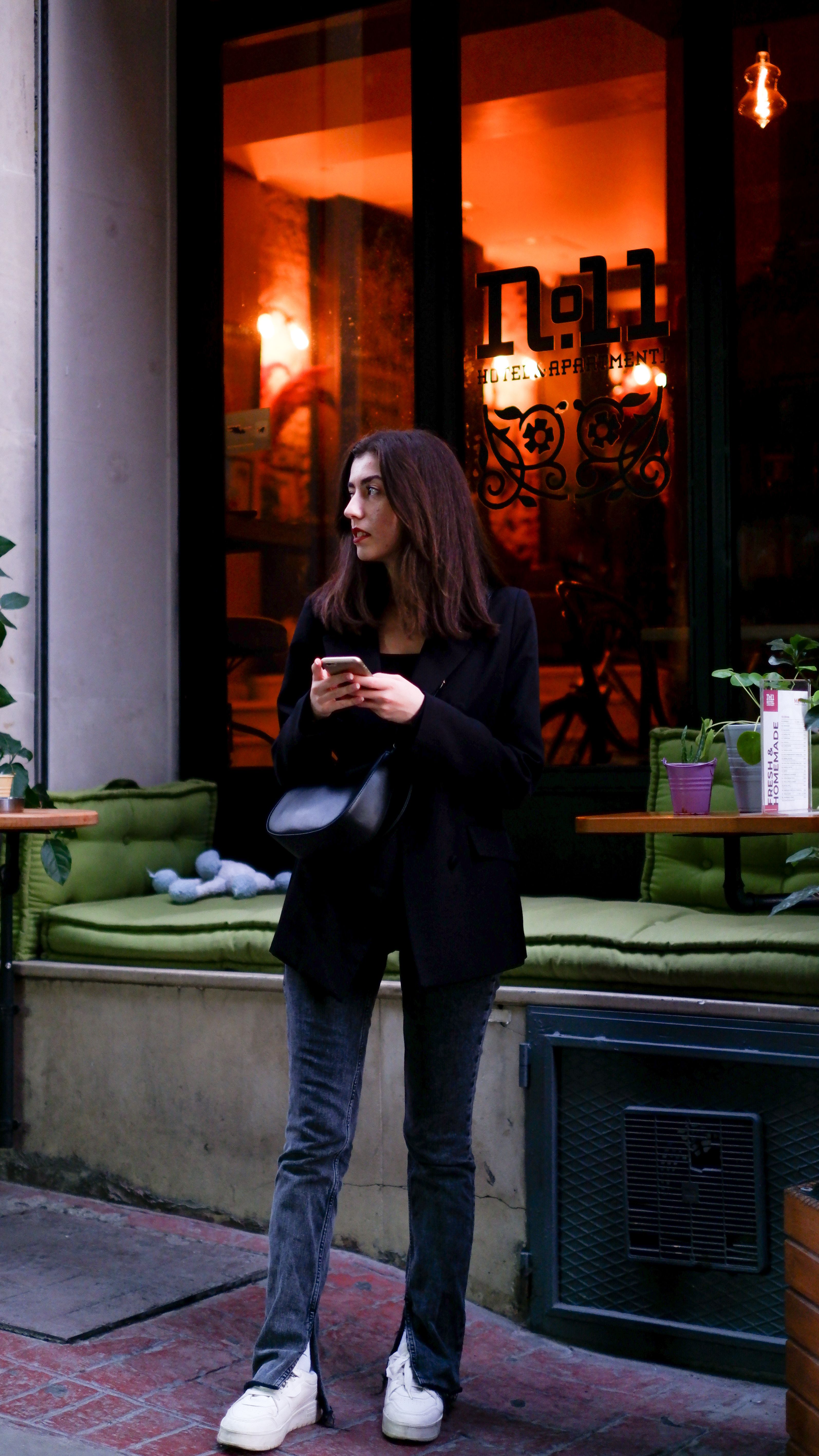 Trendy woman standing outside a cozy café, holding a phone, exuding a fashionable urban vibe.