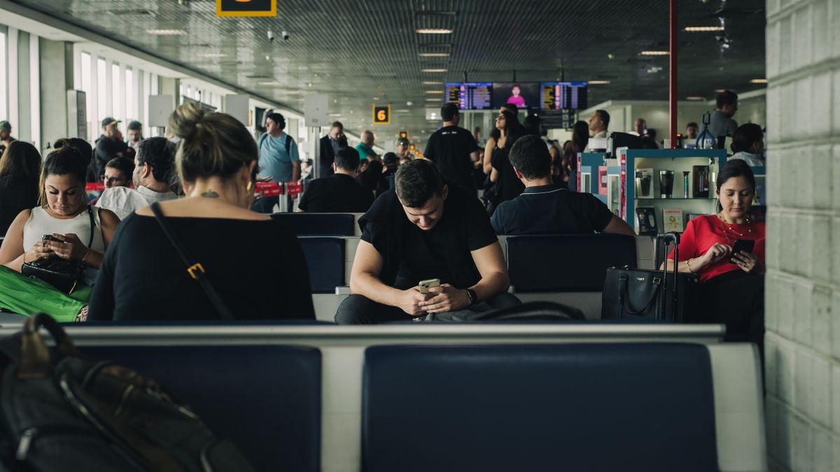 Travelers seated and waiting at São Paulo airport terminal, engaging with smartphones.