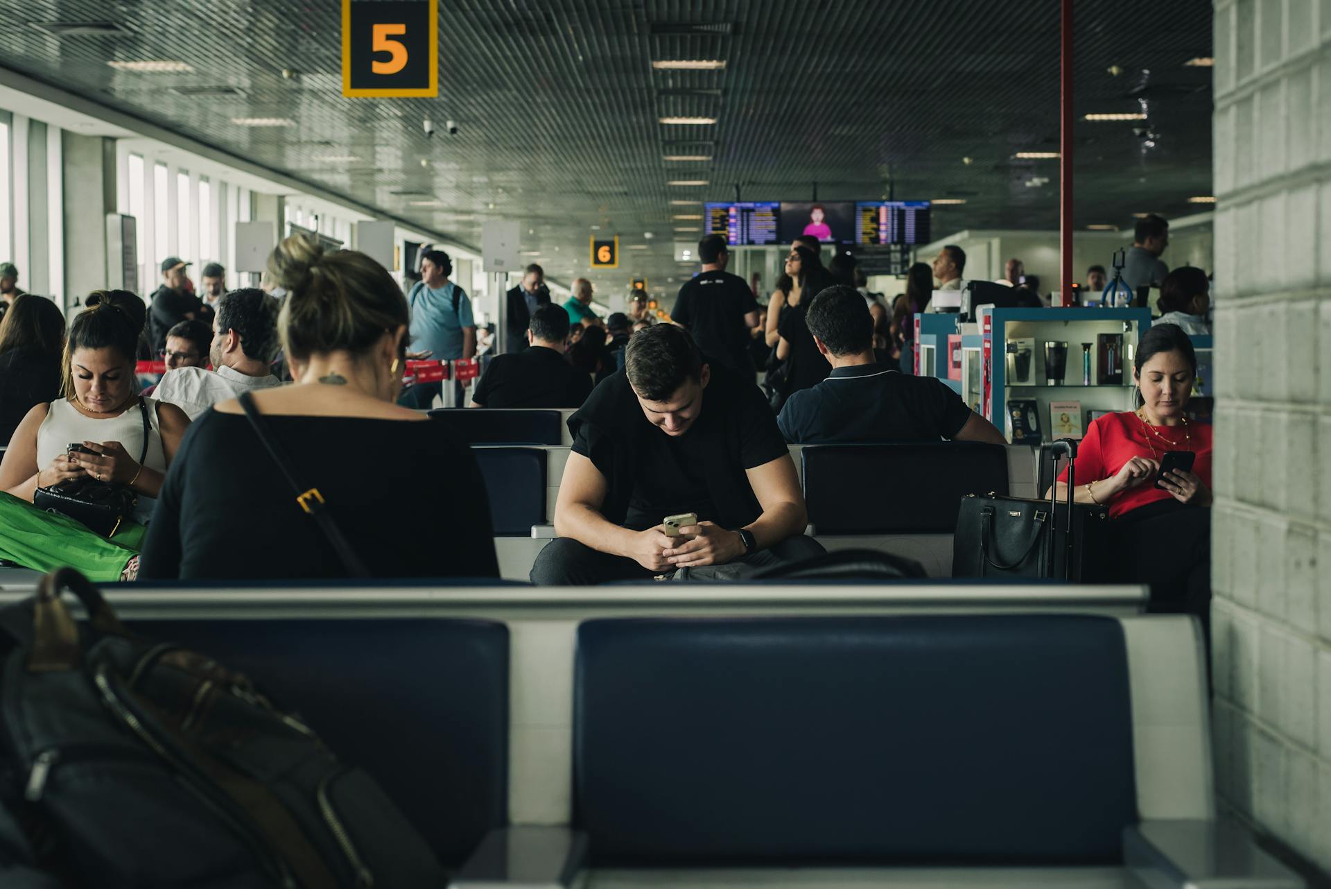 Travelers seated and waiting at São Paulo airport terminal, engaging with smartphones.